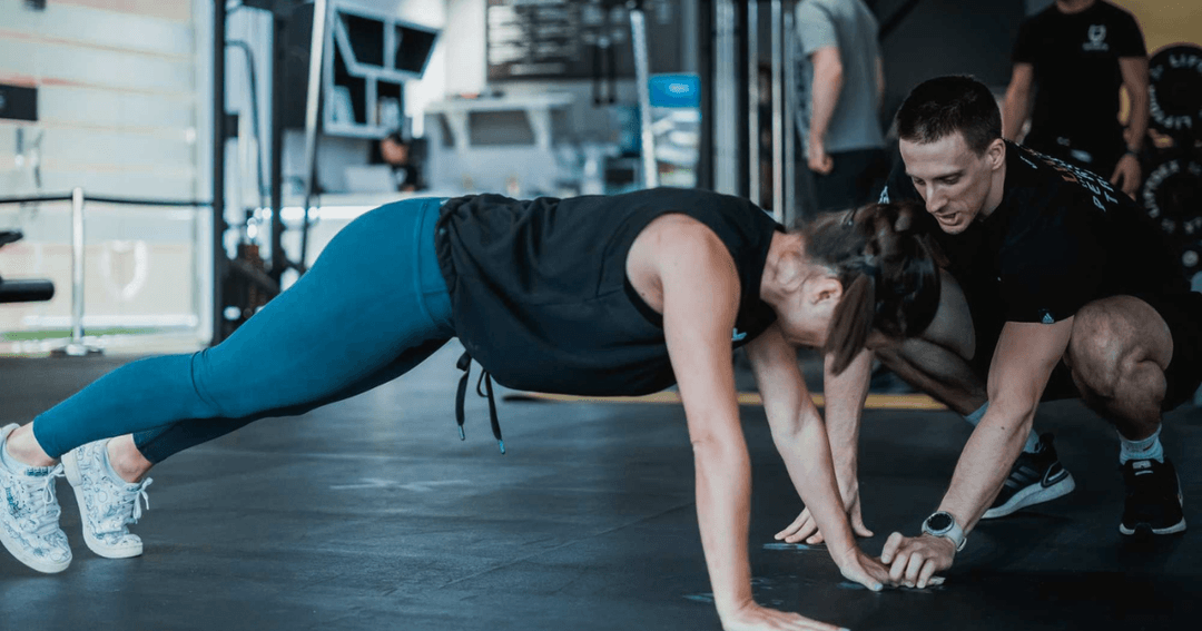 Personal trainer helping client with her form.