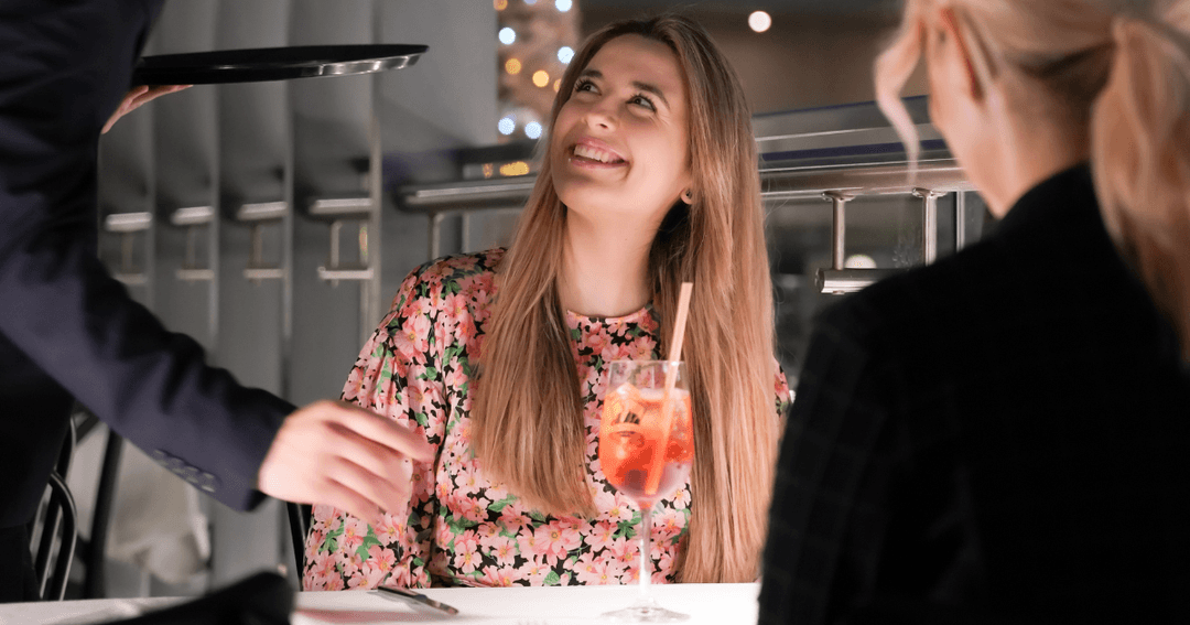 Two women getting served drinks by a waiter