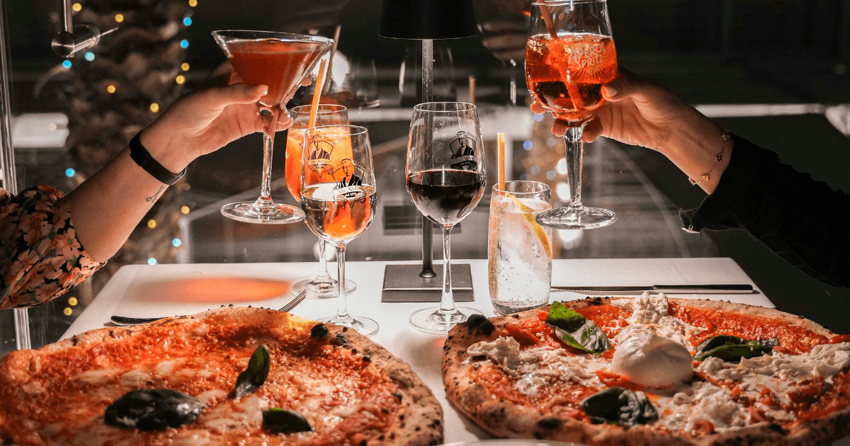 Guests toasting their drinks over a pizza