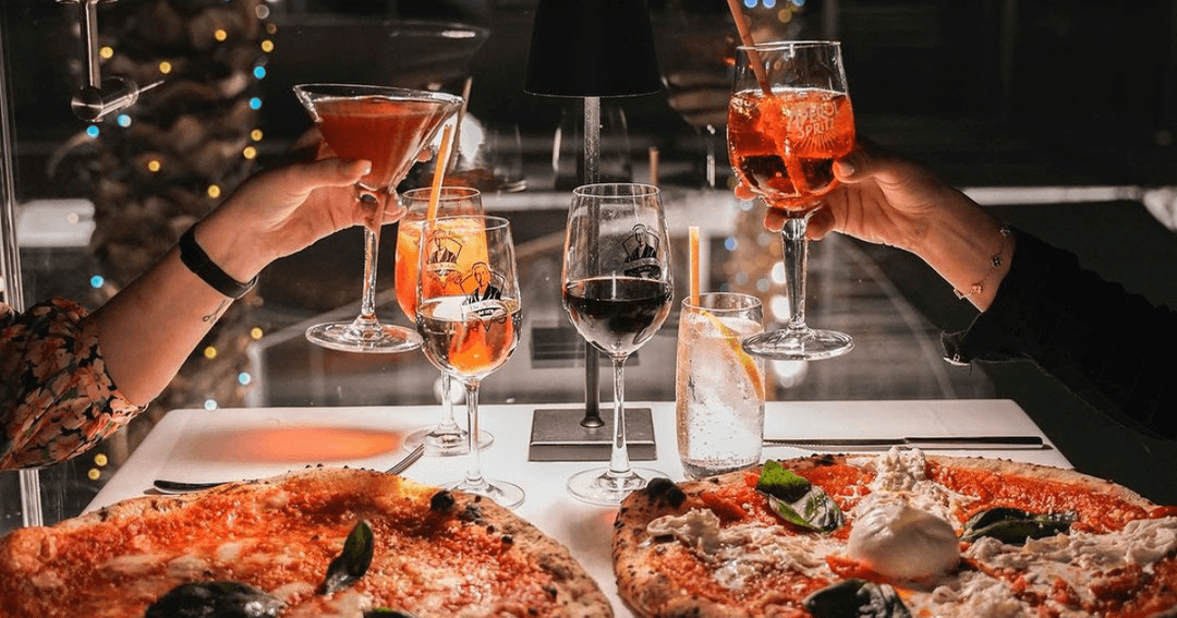 Girls toasting their drinks over pizza