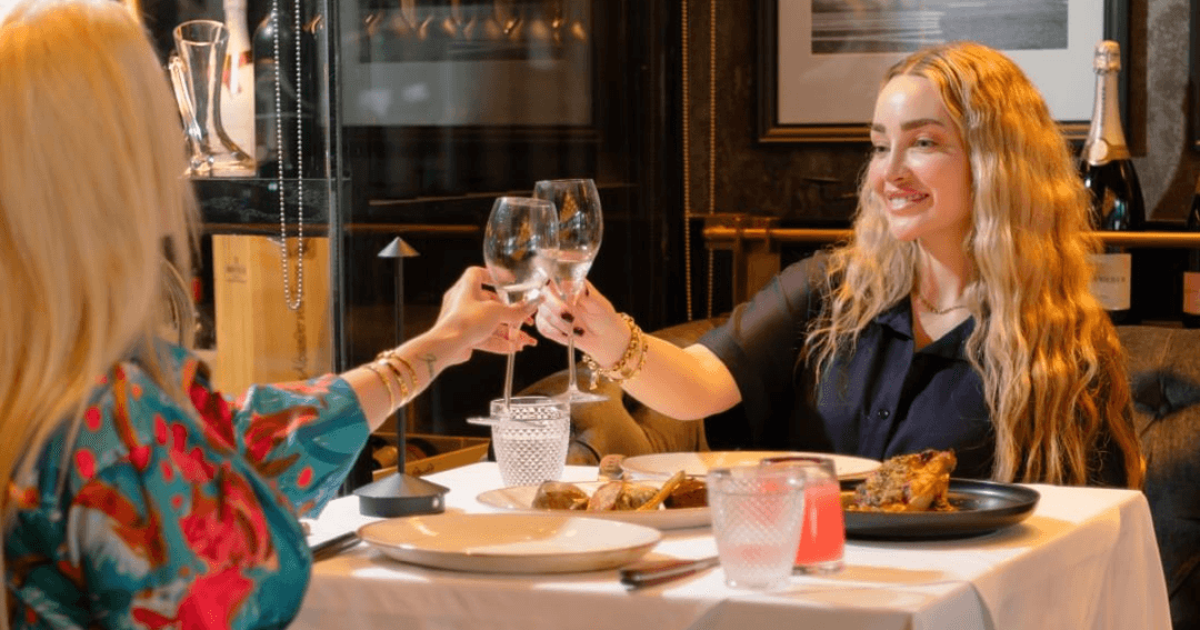 Two women toasting their glasses over food