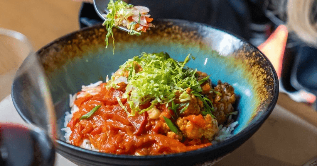 A vibrant bowl of rice topped with a flavorful tomato-based stew and garnished with fresh greens, served at Talhan Expo City.