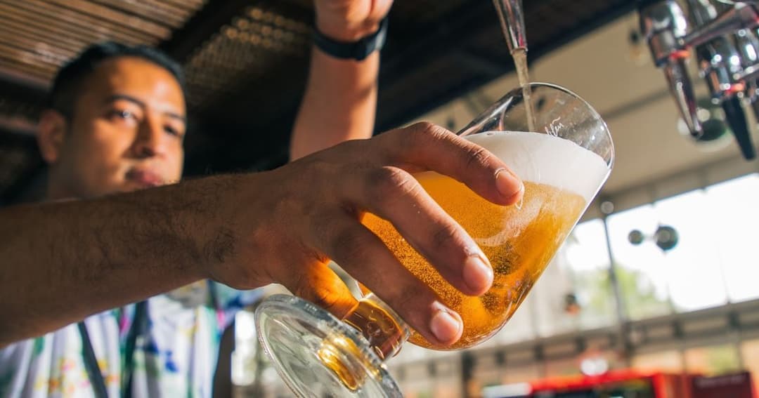 A bartender at Barasti pouring a glass of draft beer, showcasing the bar's lively atmosphere and drink offerings.