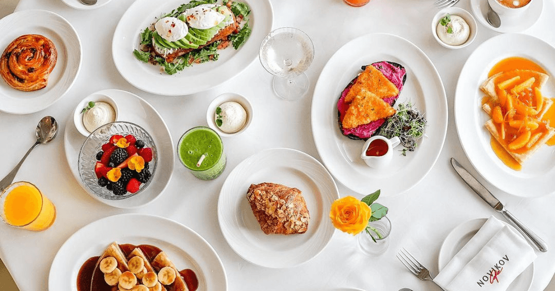 Elegant breakfast spread at Novikov Cafe in Dubai Mall, featuring avocado toast with poached eggs, fresh fruit salad, green smoothie, pastries, and a variety of gourmet dishes.