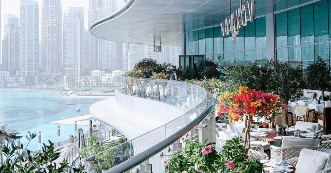 Stunning view from the terrace of Novikov Cafe in Dubai Mall, showcasing the skyline and water fountain of Dubai Mall with lush floral decor and modern dining setup.