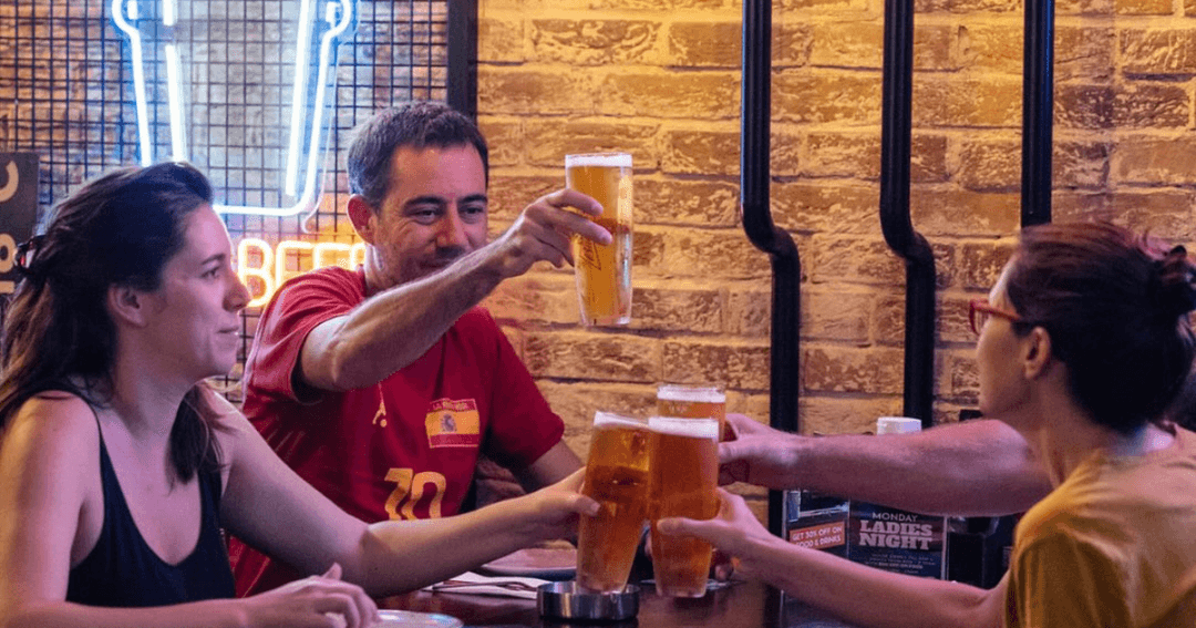 Friends cheer with beers at Brew House, capturing a lively and casual moment in a bar setting illuminated by neon lights.