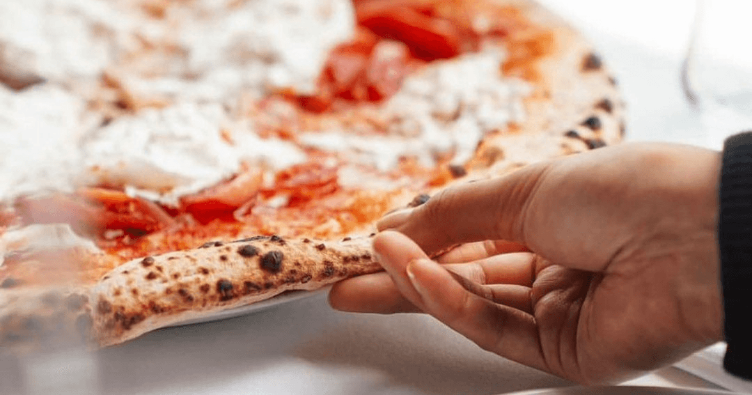 a slice of margherita pizza being picked up from plate