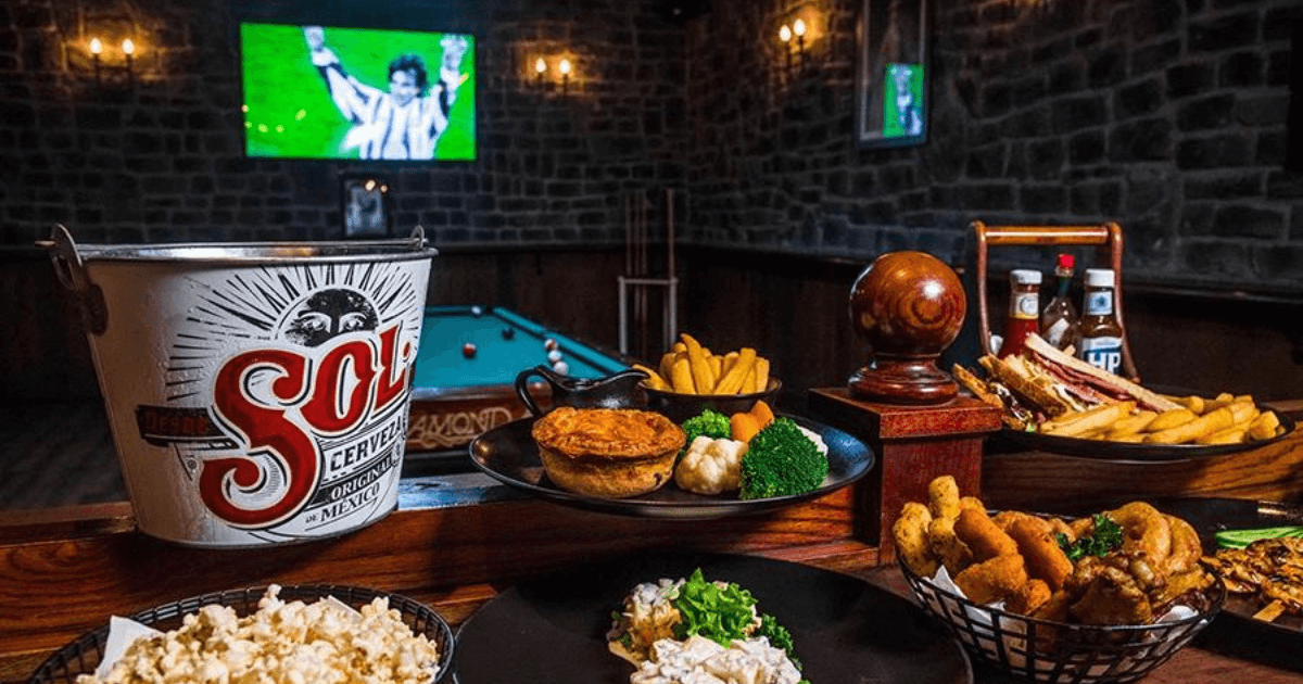 A selection of pub food with a bucket of Sol beer at Nell Gwynne in Dubai, with a pool table and sports screen in the background.