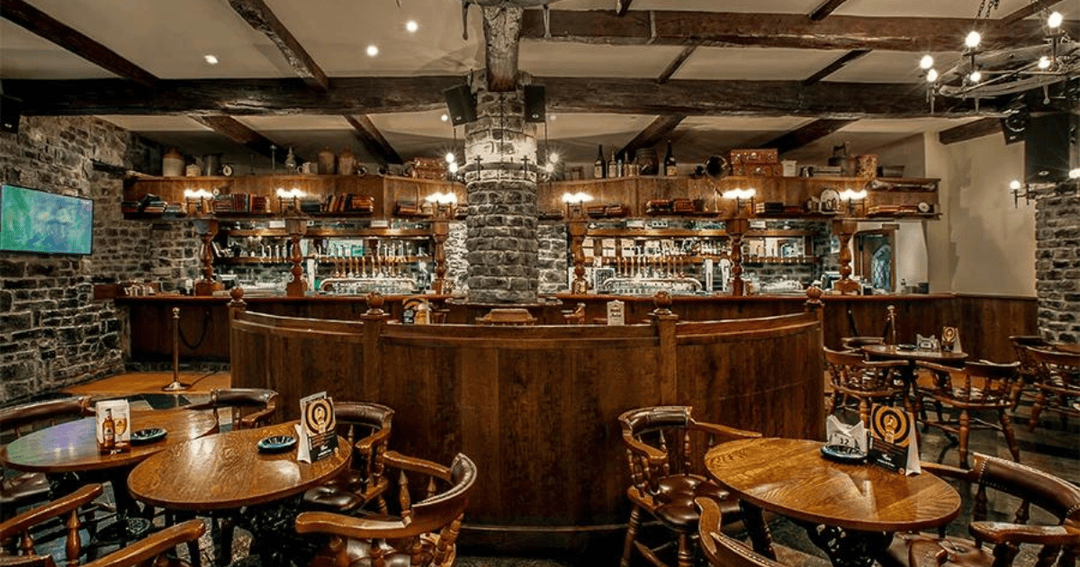 The cozy interior of Nell Gwynne pub in Dubai featuring a well-stocked bar and rustic decor.