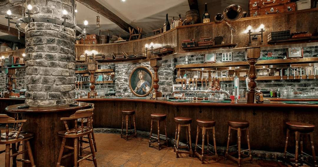 Rustic bar area with stone accents and wooden stools at Nell Gwynne pub in Dubai.