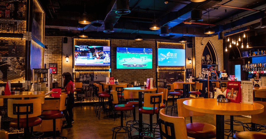 Empty tables and bar stools at Brooklyn Bar, Dubai, with multiple screens showing sports events and a relaxed ambiance.