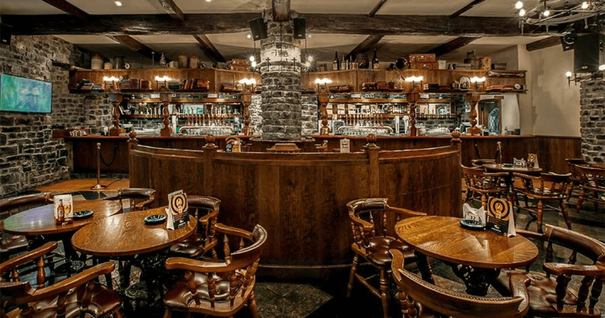 Classic wooden bar area at Nell Gwynne, featuring a stone pillar and a variety of drink selections