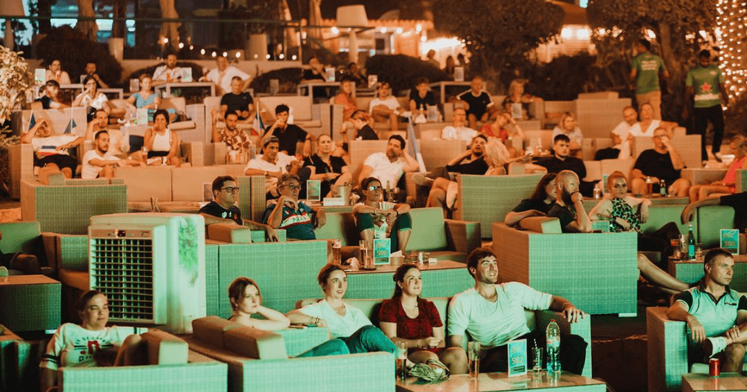 Guests watching a sports event on a big screen at Wavebreaker, Dubai, with a beachside setting and relaxed seating.